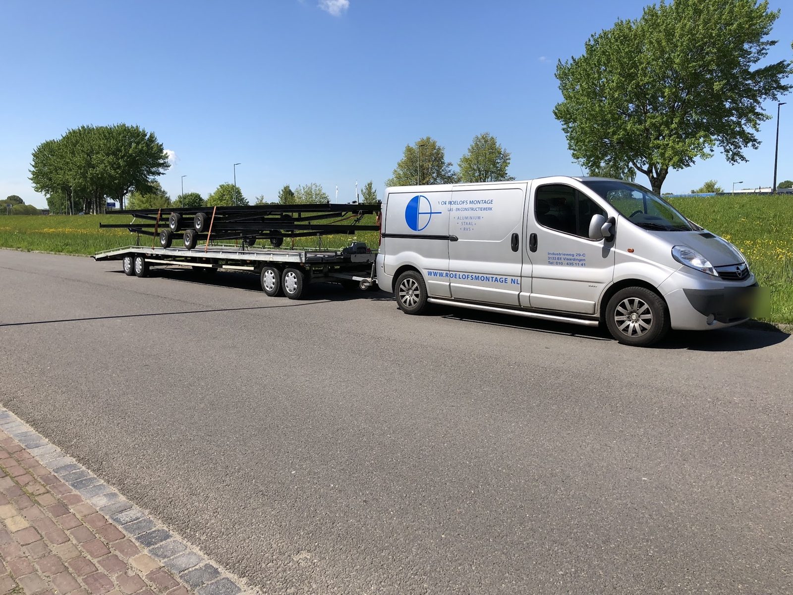 Bedrijfsbus van Roelofs Montage met een lange aanhanger vol zwarte stalen onderstellen