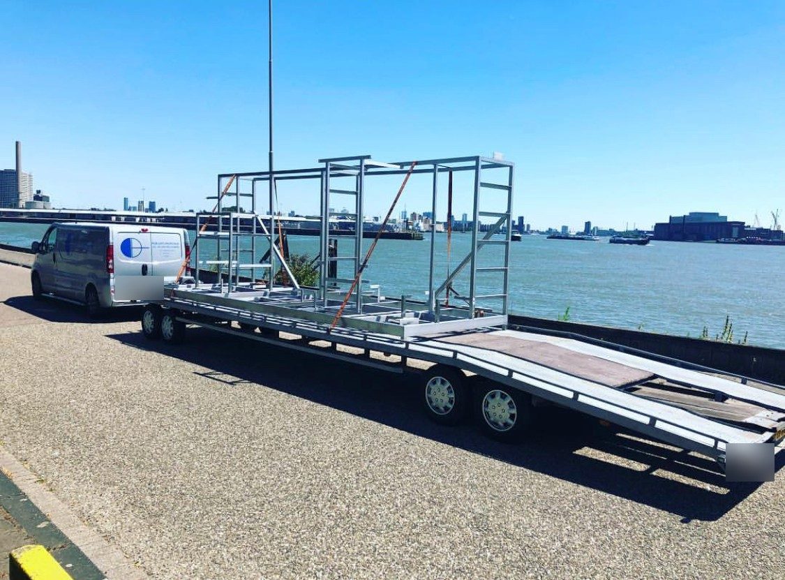 Aluminium frames op een aanhanger langs de Maas, met de bedrijfsbus ervoor